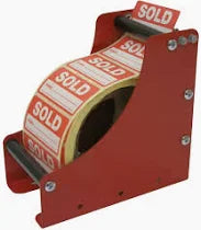 A red label dispenser with a roll of labels that have 'SOLD' printed on them, mounted on a tabletop stand.